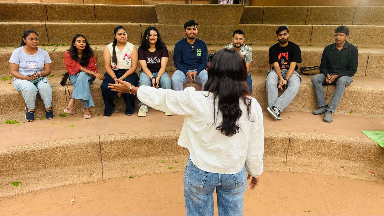 Someone standing with their arms out taking the floor at an Ithaka Home, everybody sitting on the steps turned towards them